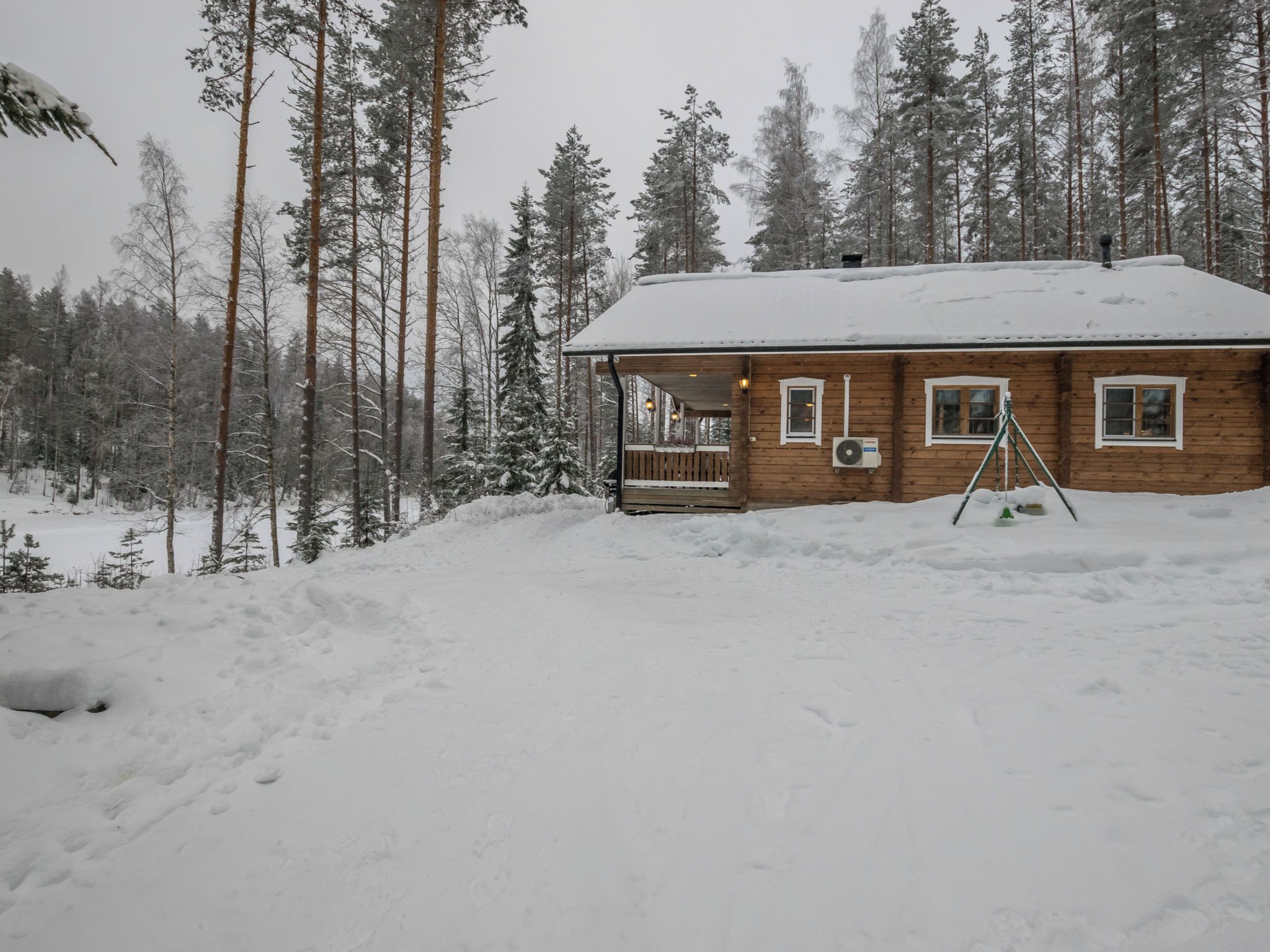 En stuga av trä med en veranda, omgiven av snötäckta träd.