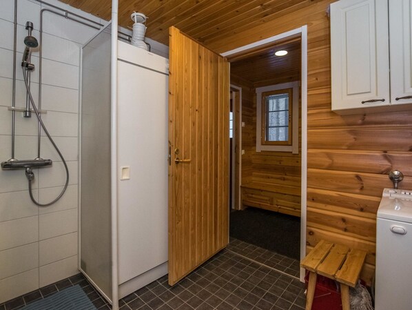 A compact bathroom with a shower, a white toilet, and a wooden door leading to another room.