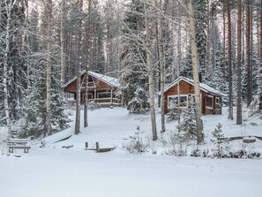 Deux cabanes en bois, entourées d’arbres couverts de neige.