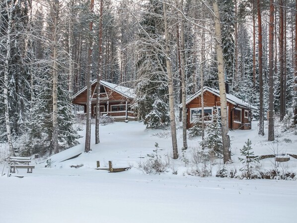 Two wooden cabins surrounded by snow-covered trees.