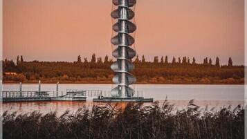 Une haute structure en spirale, située au bord d’un plan d’eau, avec une forêt en arrière-plan.