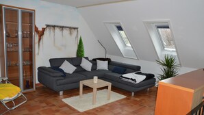 A modern living room with a sectional sofa, a small wooden table, a glass cabinet, and a plant. - A holiday house / apartment with a difference - with a sauna in the living area.  (Löbnitz)