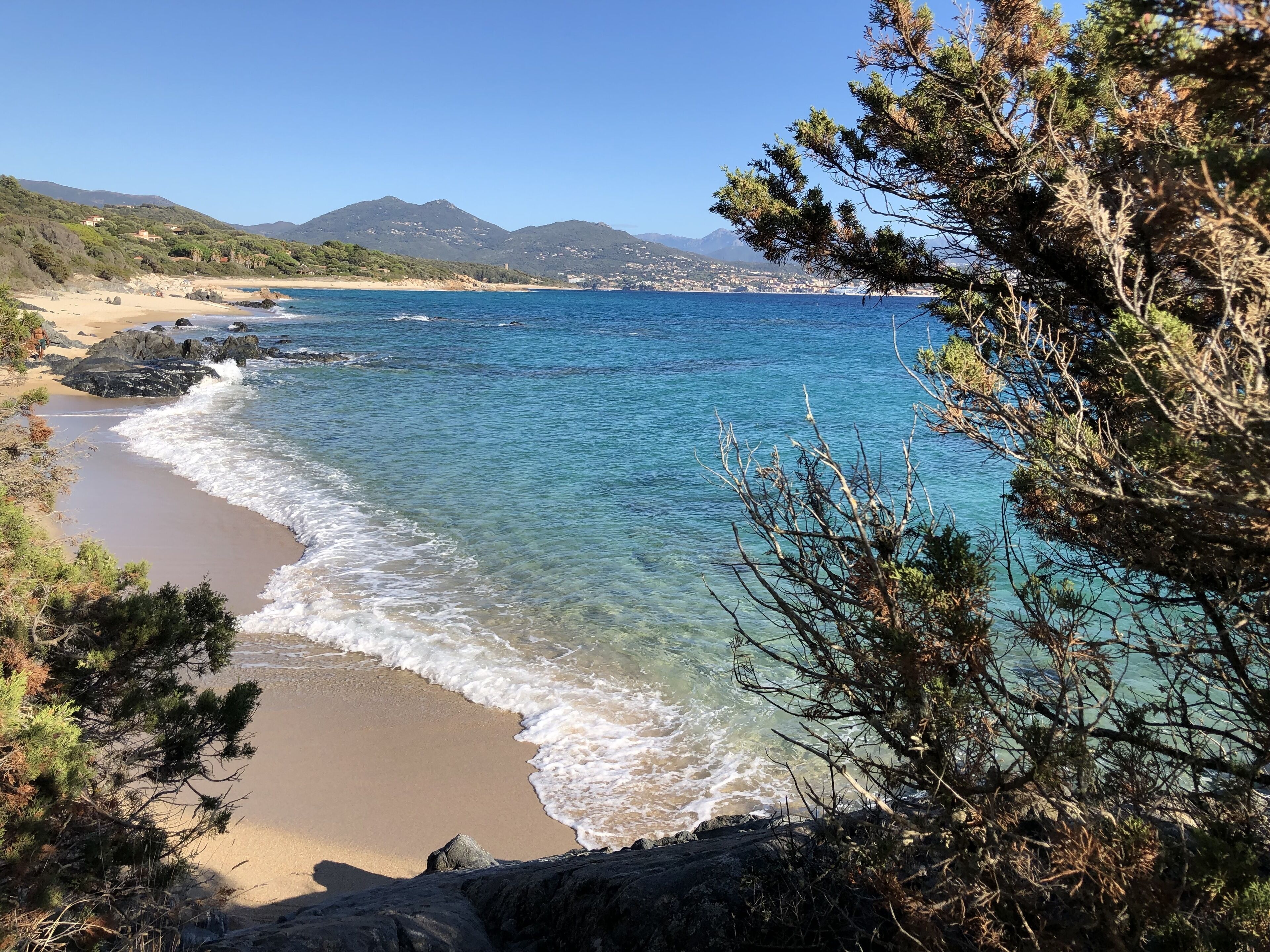 Paisaje costero con aguas azules cristalinas, playa arenosa y afloramientos rocosos.
