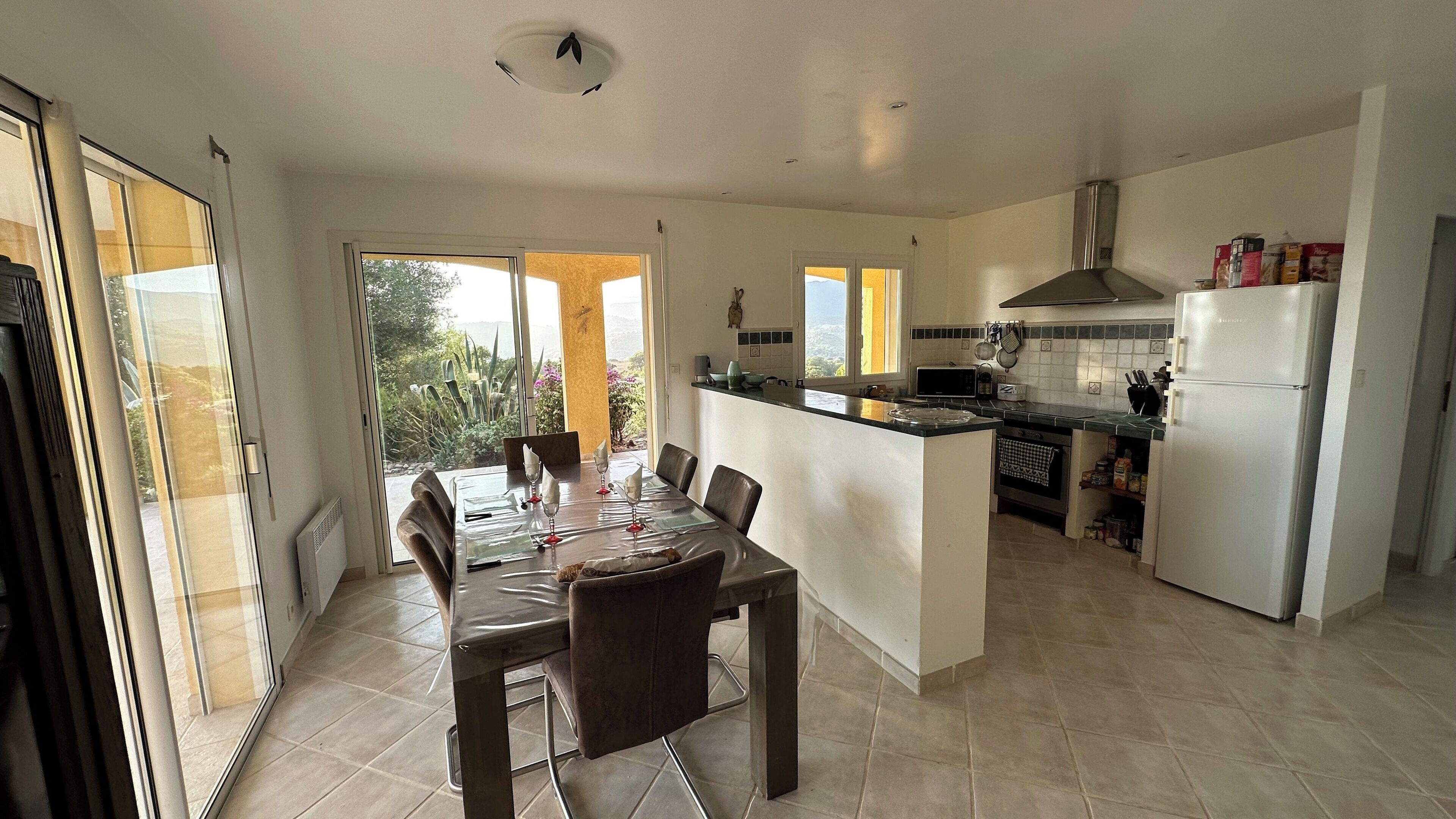 A modern kitchen with a dining area, large windows, and a view of the outdoors.