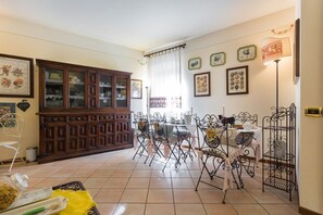 A dining area with a wooden cabinet, metal chairs, a table with a white tablecloth, and wall-mounted decorative plates. - New Day Bed & Breakfast (Assisi)