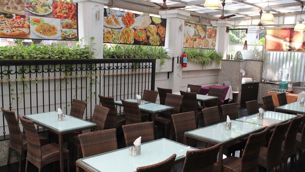 An indoor restaurant with glass tables and wicker chairs, featuring a menu on the wall and a fire extinguisher. - Hotel Park View Mumbai (Mumbai)