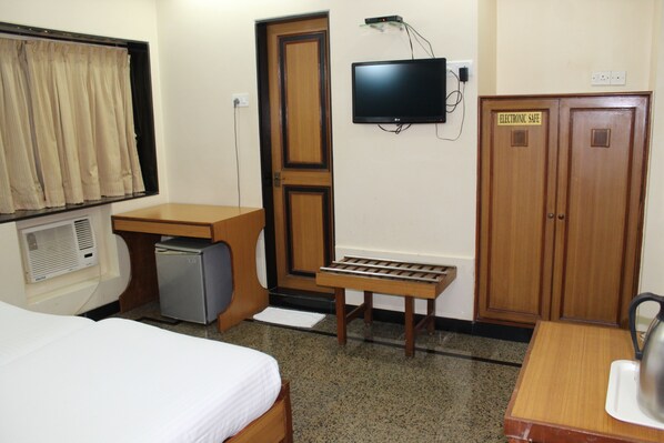 A hotel room with a bed, a desk, a television, a small refrigerator, and a cabinet marked "Electronic Safe".