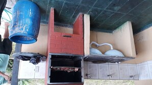 A brick-built outdoor grill with a chimney, a blue container, and a white kettle.