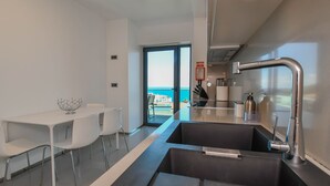 A modern kitchen with a large sink, a dining area with white chairs, and a view of the sea through a glass door. - Apartment Astrolab (Funchal / Madeira - Portugal)