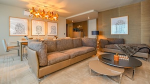 A modern living room with a large sofa, a coffee table, and a dining area. There are framed artworks on the walls and a chandelier above the seating area. - Apartment Astrolab (Funchal / Madeira - Portugal)