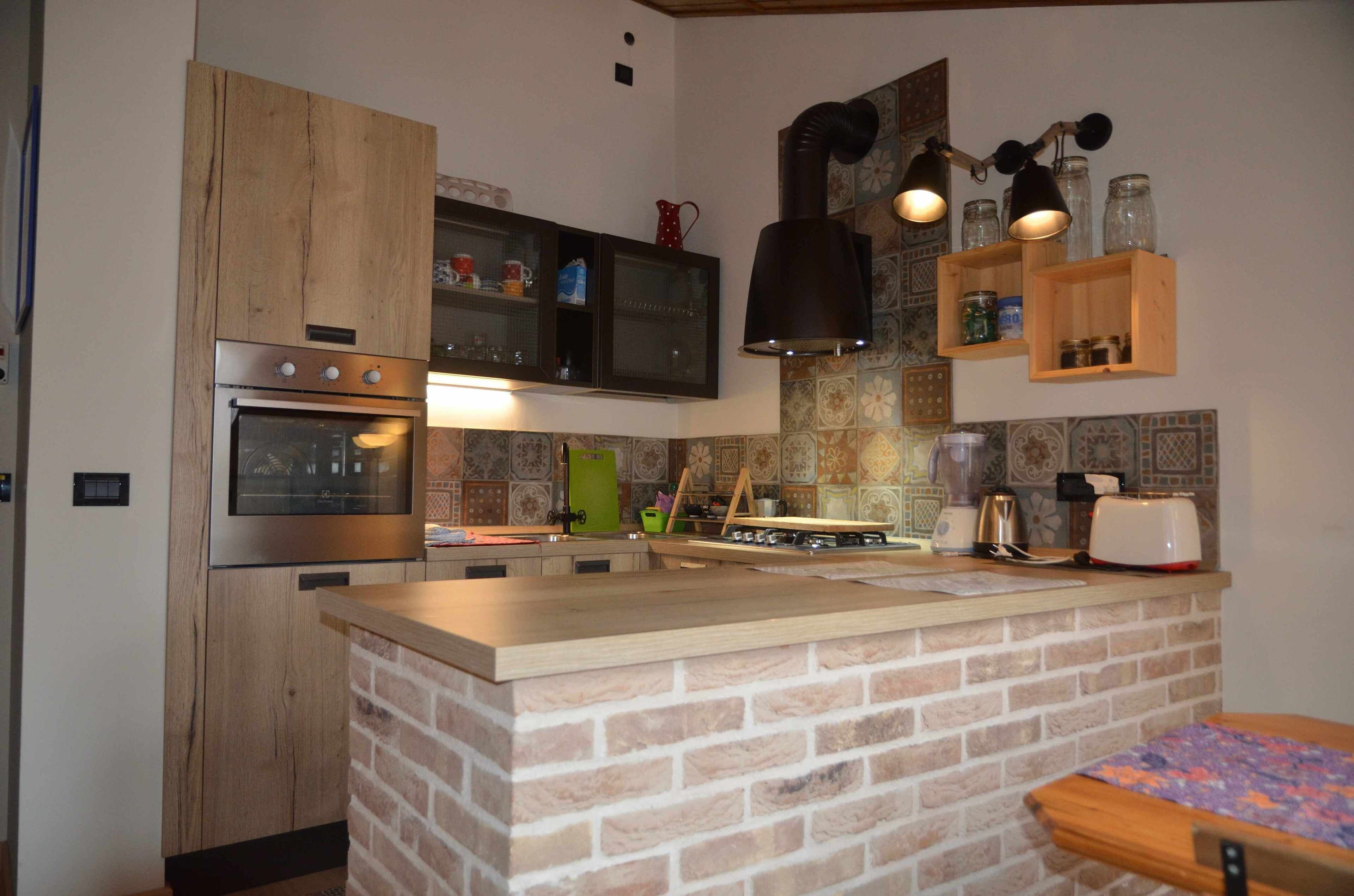 Une cuisine dotée d’un îlot central en briques, de meubles en bois, d’appareils électroménagers en acier inoxydable et d’un dosseret carrelé.
