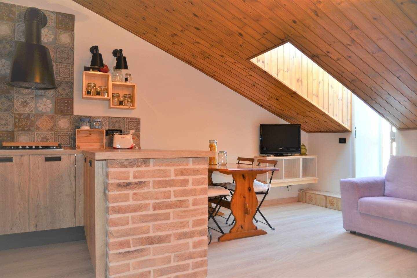 Une cuisine chaleureuse avec un plafond en bois, un coin repas avec une table et des chaises, et un téléviseur posé sur une étagère.