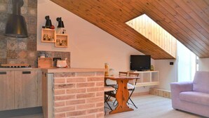Una cocina acogedora con techo de madera, un comedor con mesa y sillas, y un televisor en un estante.