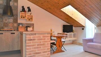 Une cuisine chaleureuse avec un plafond en bois, un coin repas avec une table et des chaises, et un téléviseur posé sur une étagère.