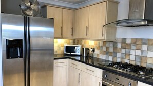A modern kitchen with stainless steel appliances, light wood cabinets, a tiled backsplash, and a gas stove.
