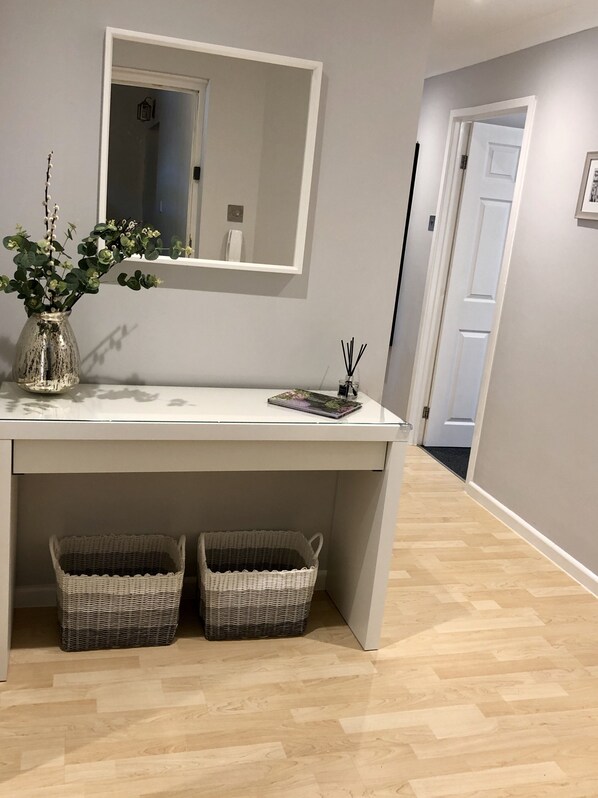 Un baño moderno con tocador blanco, un espejo, dos cestas de mimbre y un florero con follaje.