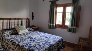 A bedroom with a wooden bed frame, a nightstand, a chair, and a window with curtains.