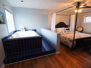 Un dormitorio con cama con dosel, baño independiente con bañera y ventilador de techo.