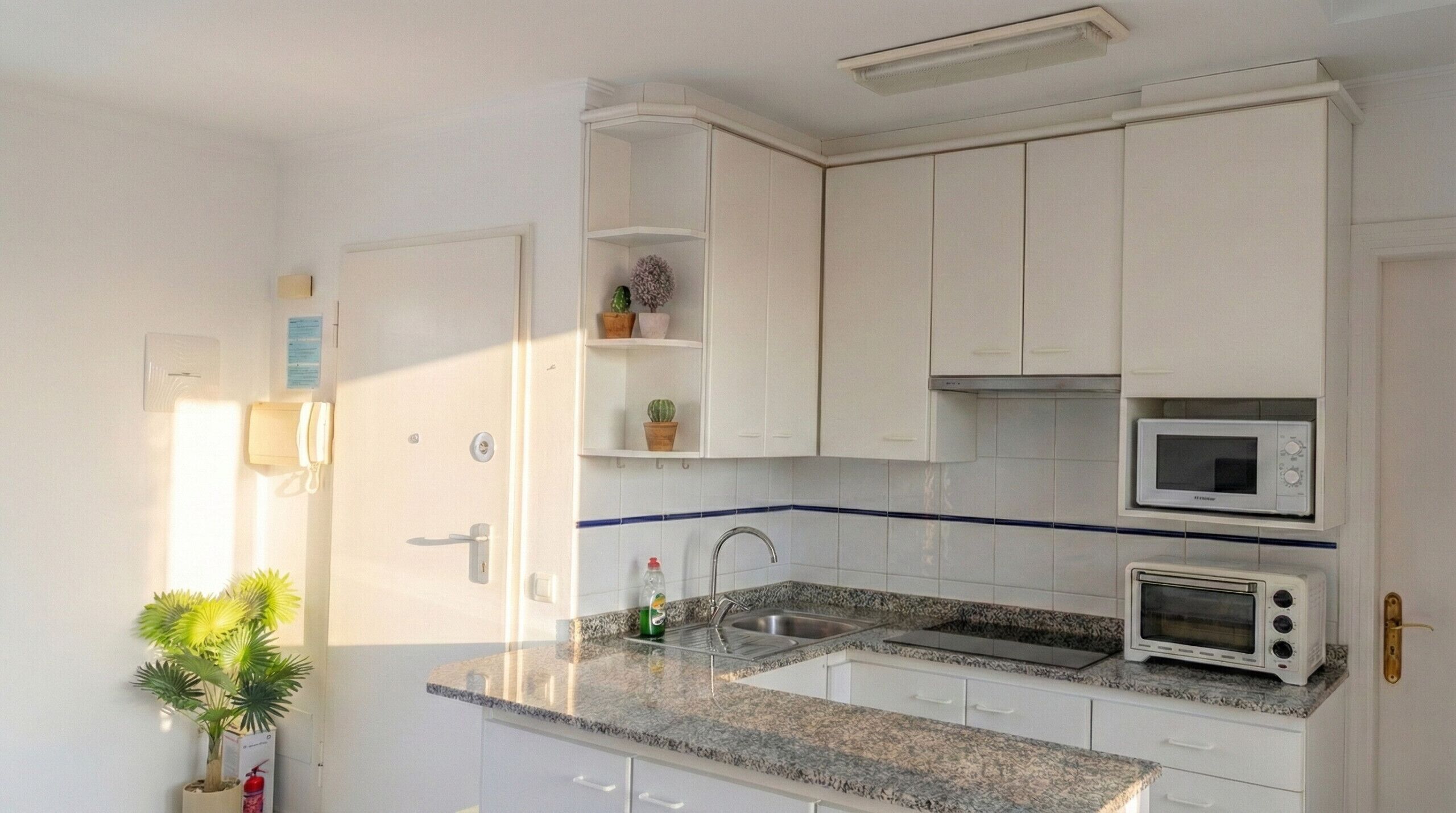 Eine Küche mit weißen Schränken, einer Granit-Arbeitsplatte, einer Mikrowelle, einem Toaster und einem Spülbecken.
