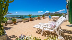Eine Terrasse mit weißen Lounge-Stühlen, Kübelpflanzen und Blick auf das Meer.