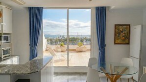 Eine moderne Küche mit einer großen Schiebeglastür, die auf einen Balkon mit Blick auf das Meer und Palmen führt.