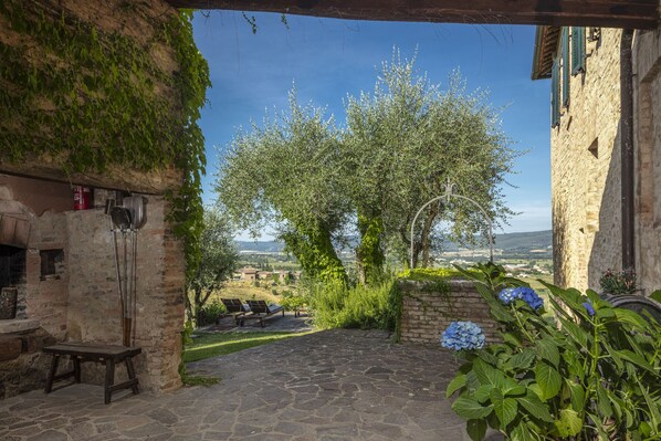 Um pátio de pedra com vista para oliveiras e paisagem distante.