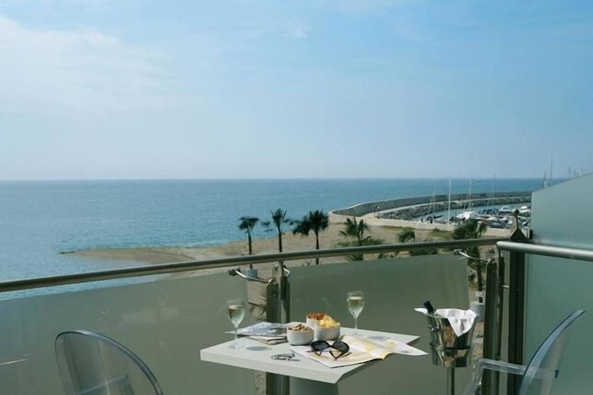 A balcony with a table set for two, overlooking a beach and ocean.