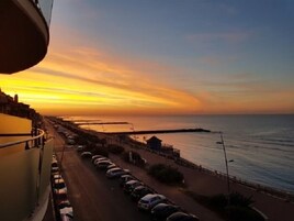 Una strada costiera con auto parcheggiate e vista sul mare al tramonto.
