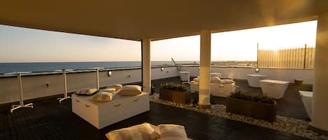 Un área de descanso al aire libre moderna con terraza de madera, sofás blancos y jardineras.