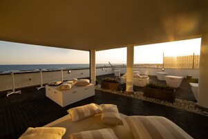 Un'area lounge esterna moderna con un pavimento in legno, divani bianchi e fioriere.