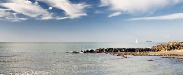 A coastal scene with a rocky breakwater, calm sea, and a distant sailboat.