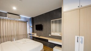 A modern hotel room with a bed, a flat-screen TV mounted on the wall, a built-in wardrobe, and a vanity with a mirror.