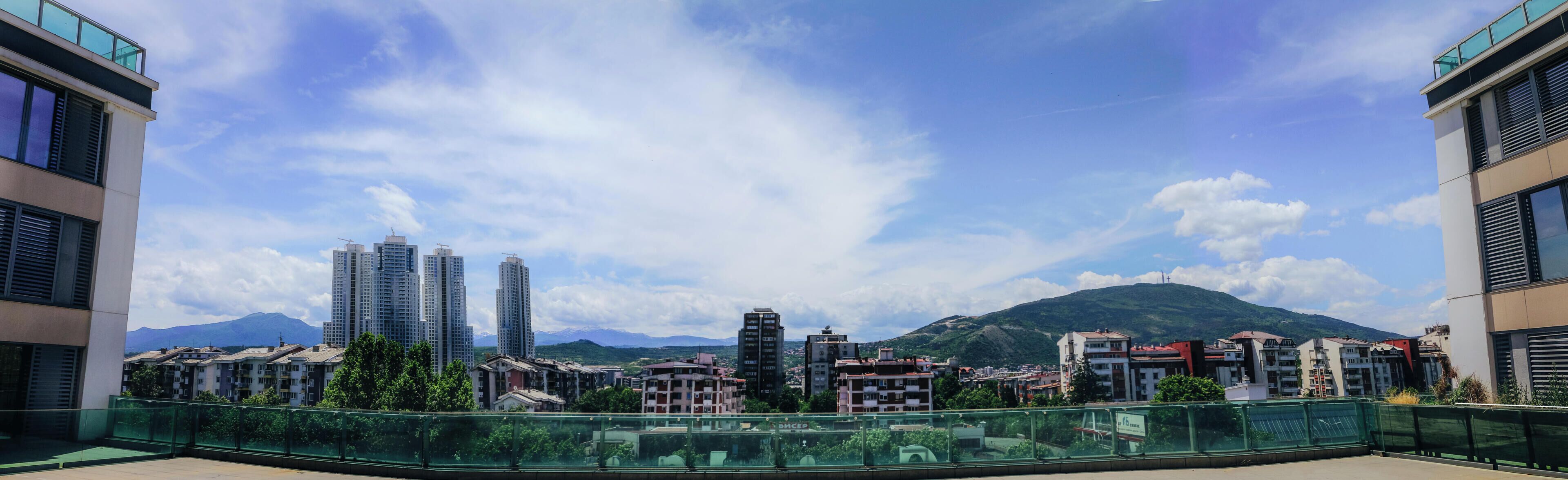 A balcony with a view of a cityscape, including high-rise buildings and a mountain in the background.