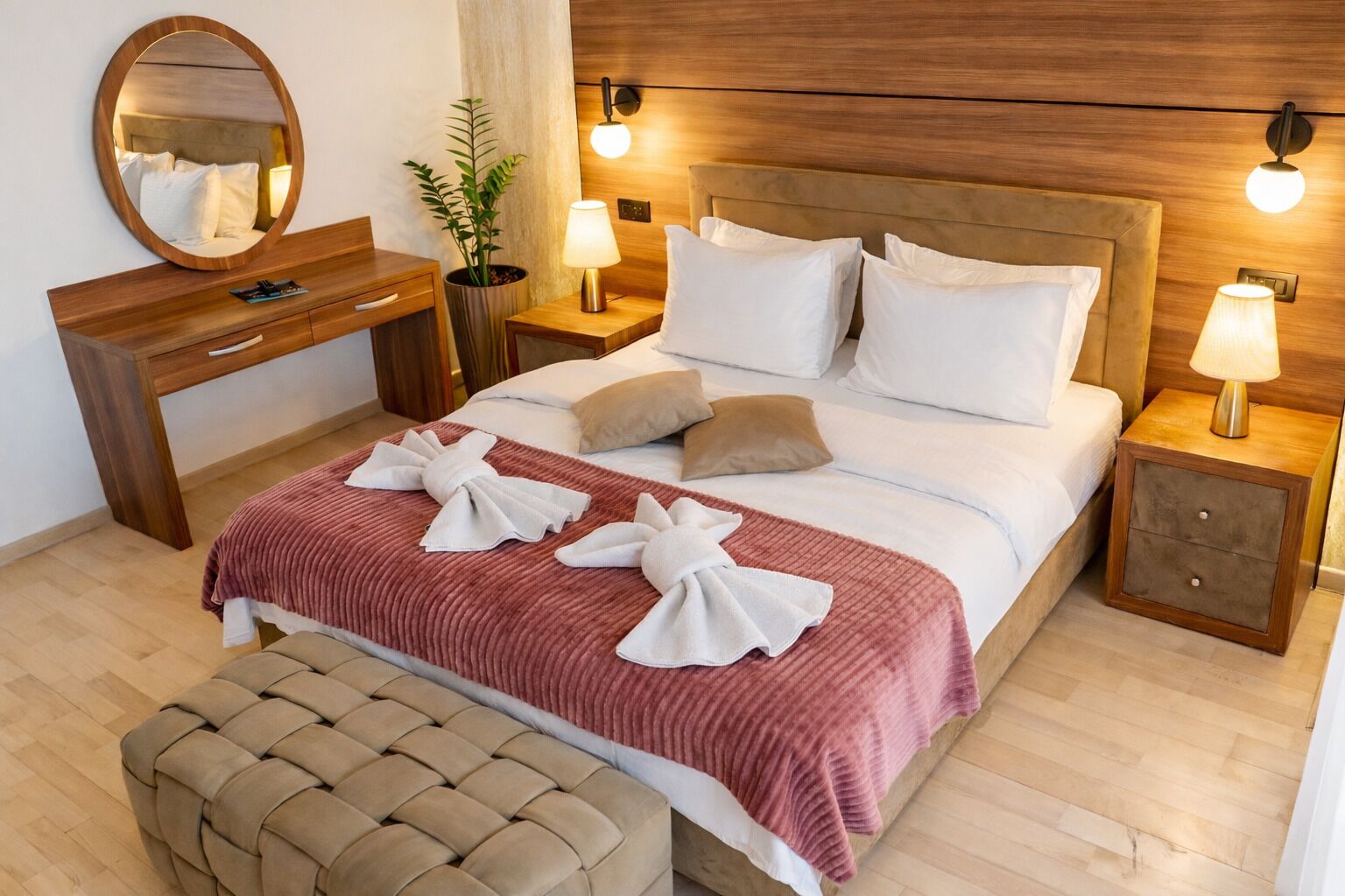 A hotel room with a bed, bedside tables, a mirror, a dresser, and a potted plant.