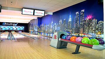 A bowling alley with a cityscape mural, multiple lanes, and a bowling ball display.