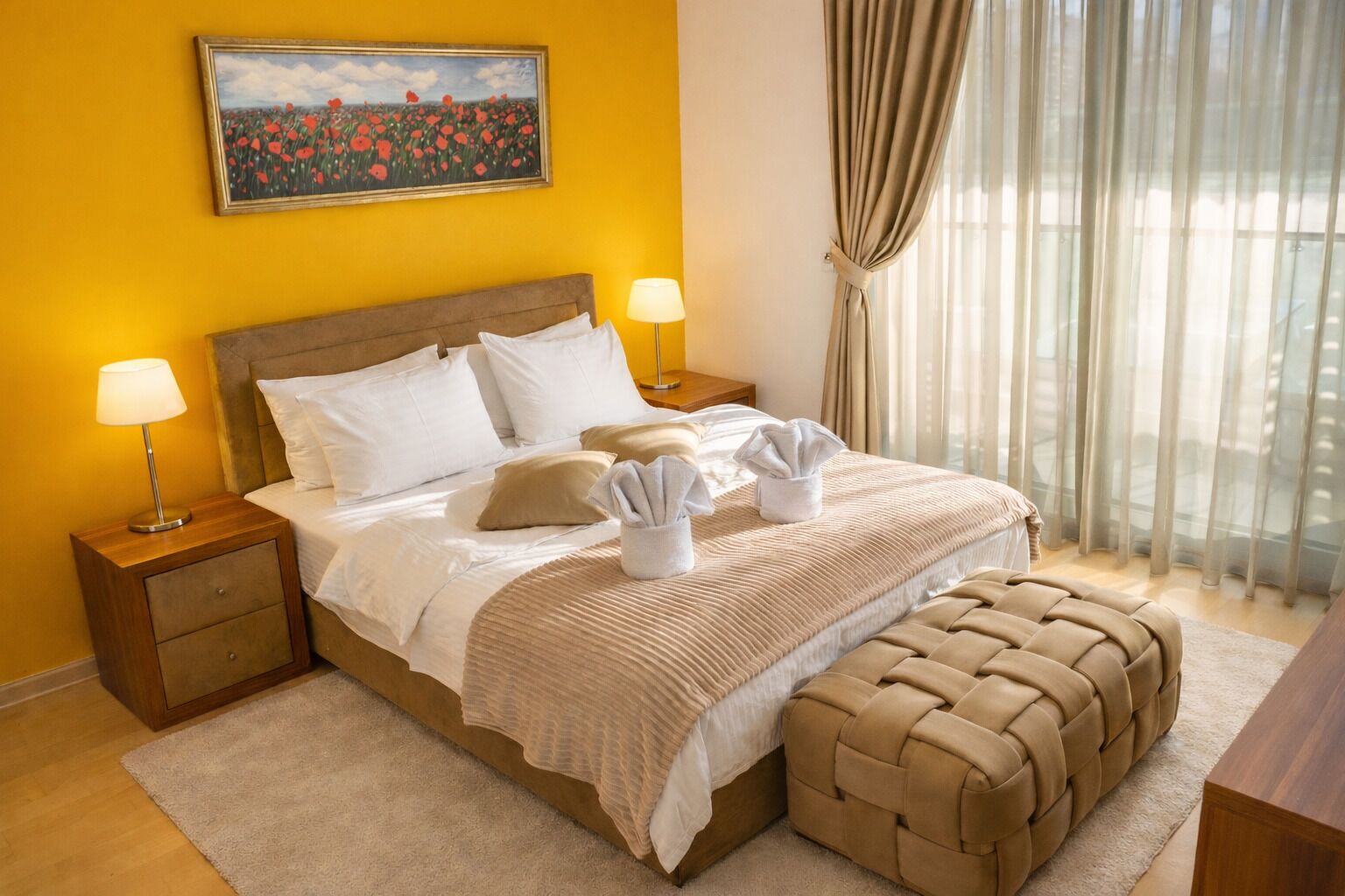 A hotel room with a bed, two bedside tables, a nightstand, a window with curtains, and a painting on the wall.