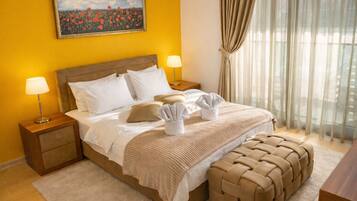 Habitación de hotel con una cama, dos mesitas de noche, una lámpara, una ventana con cortinas y un cuadro en la pared.