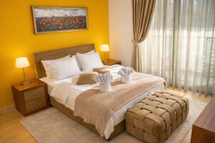 Habitación de hotel con una cama, dos mesitas de noche, una lámpara, una ventana con cortinas y un cuadro en la pared.