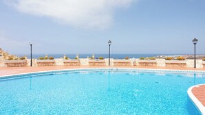 En klar blå pool med stenvæg, tre lygtestander og udsigt til havet.