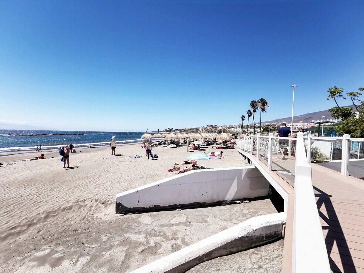 A beach with a wooden walkway, umbrellas, and people relaxing.