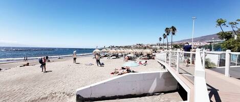 A beach with a wooden walkway, umbrellas, and people relaxing.