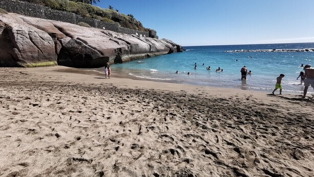 En strand med klippeformationer og klart, blåt vand.