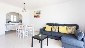 En moderne stue med en grå sofa, et sort sofabord og et spiseområde med hvide stole.