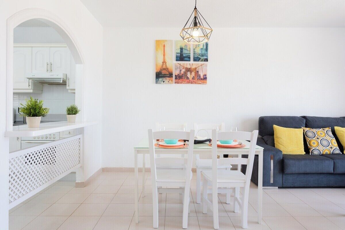 Un salon moderne comprenant un coin repas, des meubles blancs et un canapé gris agrémenté de coussins jaunes.