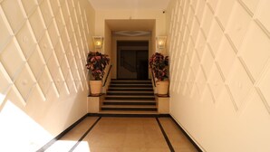 A hallway with a staircase leading to a door, flanked by two potted plants and wall-mounted lights. - Lovely balcony in Musiciens, central Nice. (Nice)