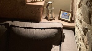 Une pièce chaleureuse avec un mur en pierre, une petite étagère en bois ornée d’une tête de cerf et d’une lanterne, et un tableau encadré accroché au mur.