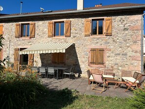 A stone building with wooden shutters, a patio with outdoor furniture, and a striped awning.