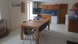 Un grand espace à manger avec une table et des chaises en bois, une cuisine dotée de meubles en bois et d’un lave-vaisselle, et un sol carrelé.