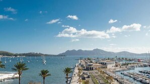 A marina with boats, a building with arches, and palm trees. - Eolo Affiliated by FERGUS (Pollenca)