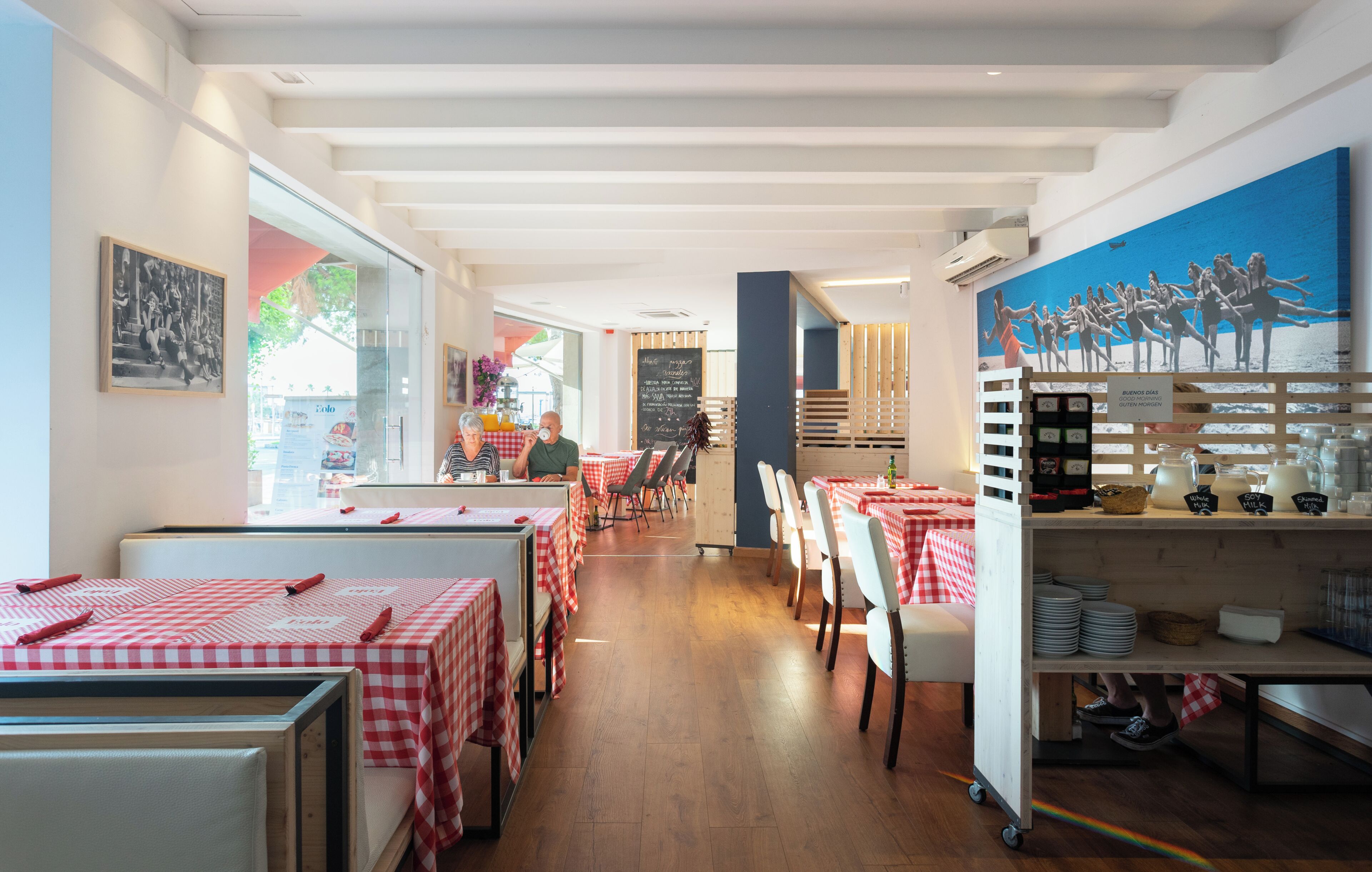 A restaurant interior with checkered tablecloths, wooden flooring, and a mural on the wall.